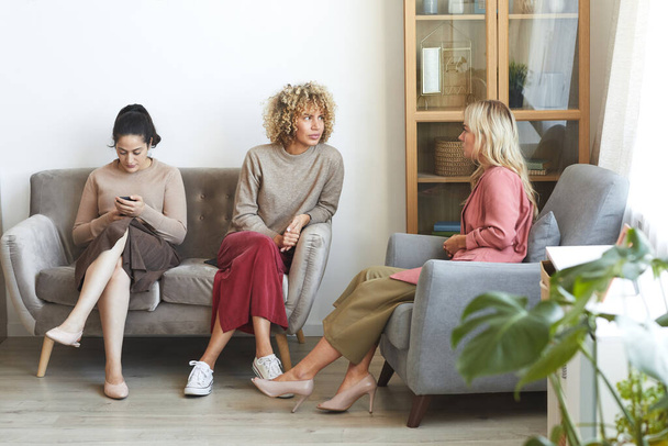 Портрет трьох сучасних дорослих жінок, які спілкуються, сидячи на дивані під час вечірки в приміщенні з друзями
 - Фото, зображення