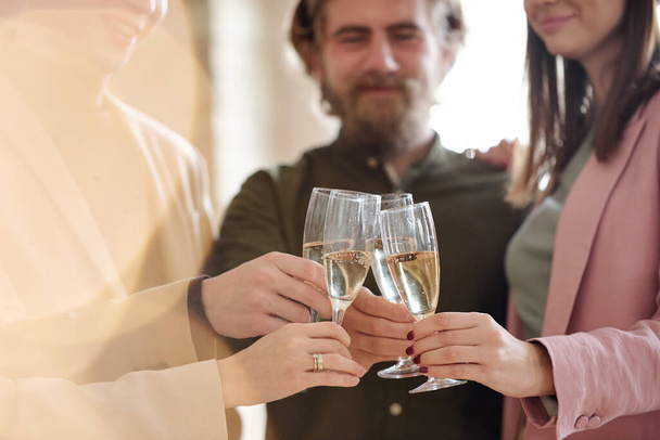 Handen van jonge collega 's in slim casualwear klinkend met fluiten champagne tijdens toast voor nieuwe zakelijke samenwerking in het komende jaar - Foto, afbeelding