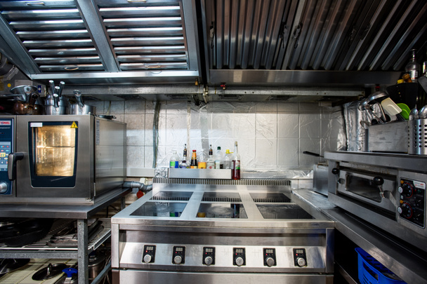 Parte del interior de la gran cocina del restaurante contemporáneo que incluye estufa eléctrica y horno para hornear y asar alimentos, utensilios de cocina - Foto, imagen