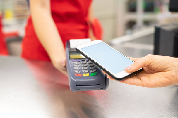 Nahaufnahme einer unkenntlichen jungen Frau, die Online-Banking-Technologie auf dem Smartphone nutzt, um im Geschäft Waren zu bezahlen - Foto, Bild