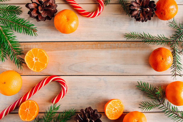 New Year's decor. Christmas tree branches, pine cones, tangerines and candies on a wooden background. - Фото, изображение