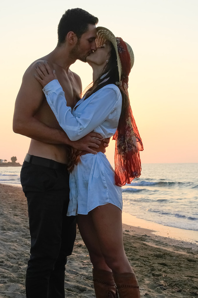 幸せな若いカップル優しく抱きしめると夕暮れ時のビーチでキス. - 写真・画像