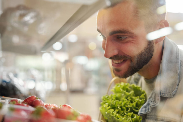 Gıda reyonunda durup akıllı telefon uygulaması ile yiyecek listesini kontrol eden ceketli, ciddi genç sakallı bir adam. - Fotoğraf, Görsel