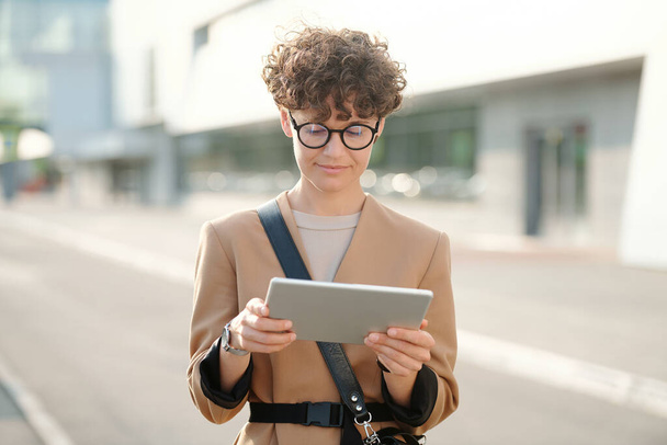 Jonge mooie brunette zakenvrouw met digitale tablet kijken business webinar of conferentie tegen de weg in stedelijke omgeving - Foto, afbeelding