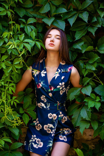 Teenager girl in blue flowers dress on green ivy background - Fotó, kép