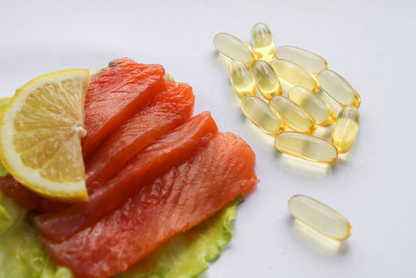 Omega-3 visolie capsules in de vorm van vis en zalm filet plak met citroen en sla blad. - Foto, afbeelding