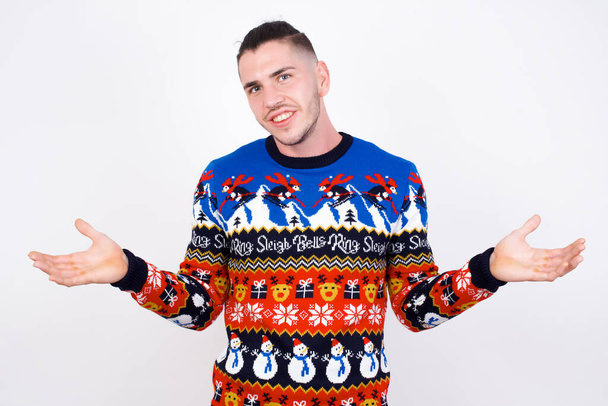 それで どうした? 白い壁にクリスマスのセーターを身に着けている傲慢な白人男性の肖像画は,無関心にガスをかける笑顔で,明白な何かを伝えます. - 写真・画像