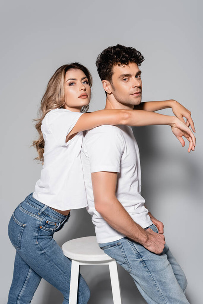 vue latérale du jeune couple en t-shirts blancs câlins isolés sur gris - Photo, image