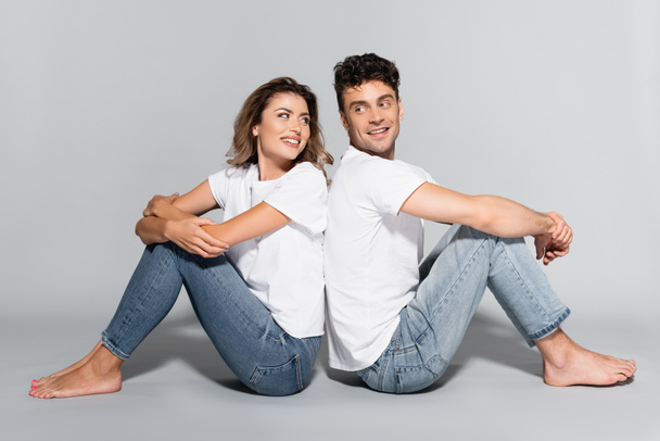 jovem casal em camisetas brancas e jeans posando de costas para trás isolado em cinza - Foto, Imagem