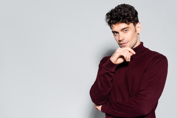 young man in burgundy turtleneck jumper posing isolated on grey - 写真・画像