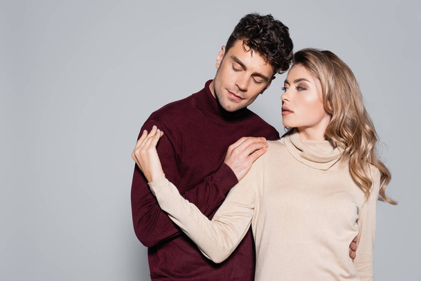 casual young couple in turtleneck jumpers embracing isolated on grey - Foto, Imagen