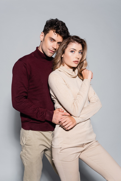 casual young couple in turtleneck jumpers embracing isolated on grey - 写真・画像