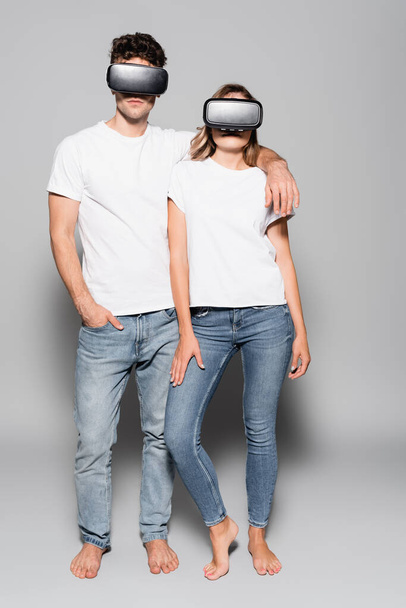 casual young couple in white t-shirts and vr headsets isolated on grey - 写真・画像
