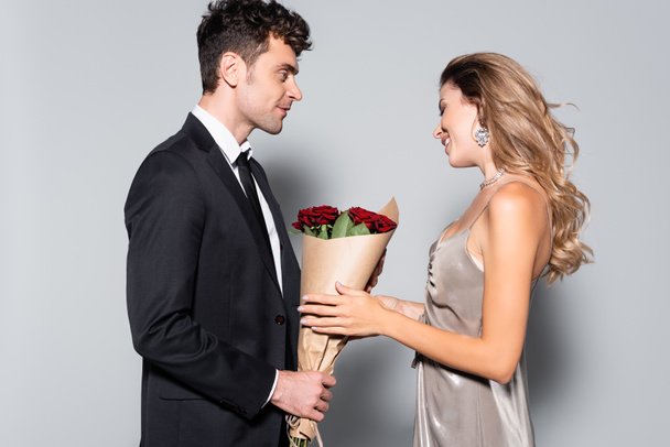 elegant young man gifting bouquet to woman isolated on grey - Valokuva, kuva