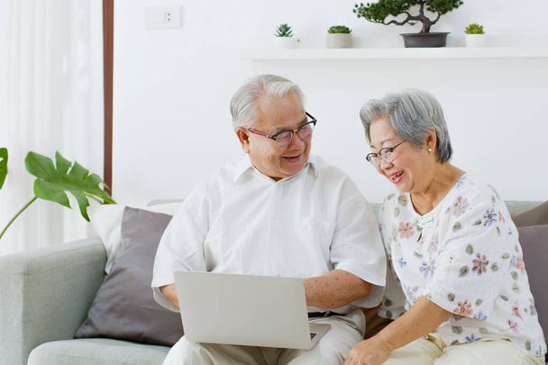 Asiatisches Senioren-Paar nutzt Computer-Laptop für Internet-Suche, Online-Shopping und Versicherungskauf im heimischen Wohnzimmer, Senior mit Technologiekonzept - Foto, Bild