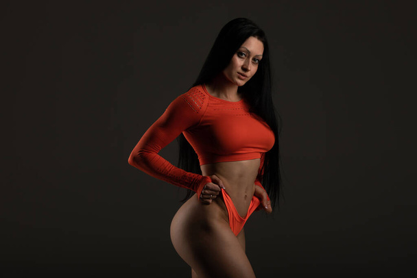 Fit woman with dark long hair in orange lingerie posing in studio looking at camera - Photo, image