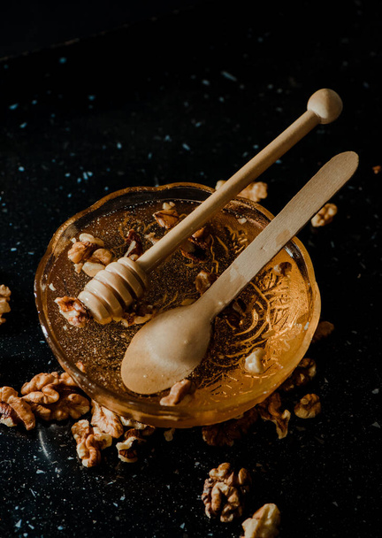 The honey in a glass bowl with walnuts and wooden spoons - Fotoğraf, Görsel