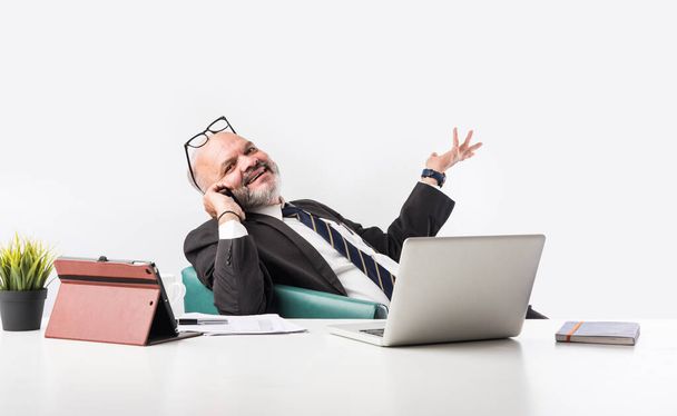 Retrato de um empresário indiano asiático sênior satisfeito sentado no local de trabalho em frente ao computador e olhando para a câmera enquanto relaxa. Velho profissional homem pés na mesa de escritório - Foto, Imagem