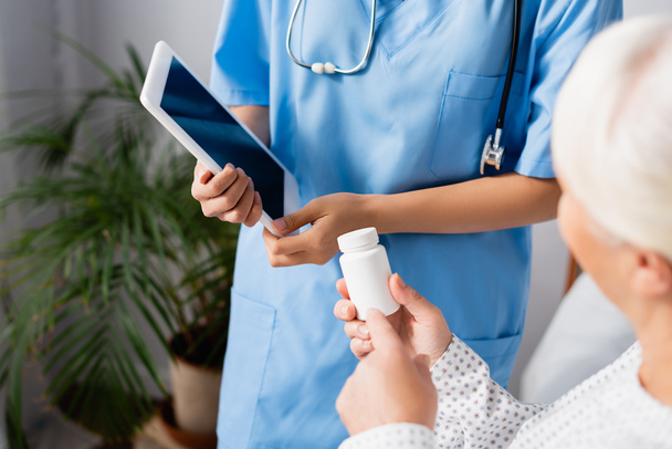 обрізаний вид на літню жінку, вказуючи пальцем на тарілку для таблеток біля медсестри, що тримає цифровий планшет
 - Фото, зображення