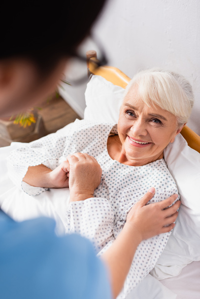 overhead view of nurse touching smiling elderly woman, blurred foreground - Fotoğraf, Görsel