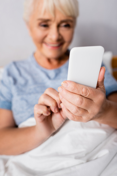 neşeli yaşlı kadın hastanede akıllı telefondan konuşuyor, geçmişi bulanık. - Fotoğraf, Görsel
