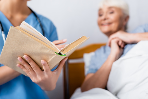 libro della lettura dell'infermiera alla donna anziana eccitata in clinica, primo piano offuscata - Foto, immagini