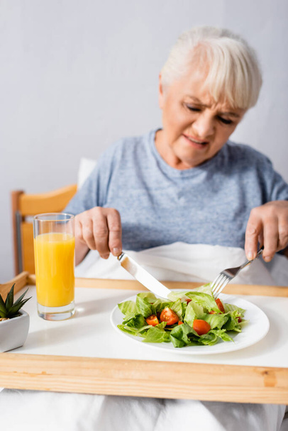 displeased aged woman having breakfast in hospital, blurred foreground - Photo, Image