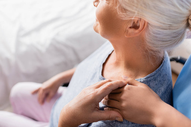 обрезанный вид медсестры, трогающей плечо пожилой женщины в больнице, размытый фон - Фото, изображение