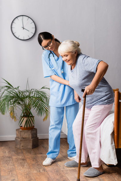 mujer asiática ayudando a una mujer anciana con bastón de caminar levantándose de la cama en el hospital - Foto, imagen