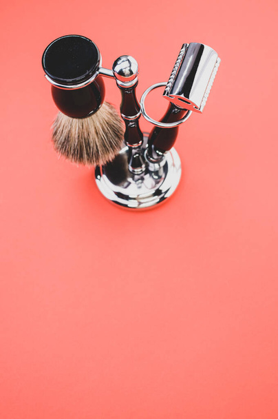 A vertical shot of a shaving brush and a razor on a red background - Zdjęcie, obraz