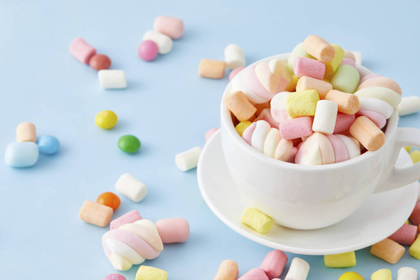 A top view closeup of a cup filled with colorful marshmallows isolated on a blue background - Fotó, kép