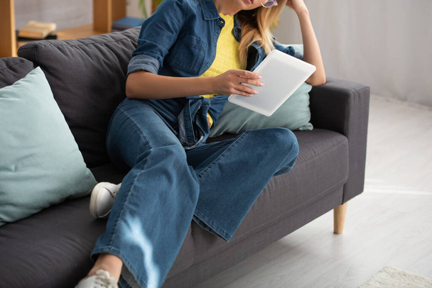 Vista recortada de la mujer joven con tableta digital en el sofá en casa sobre fondo borroso - Foto, Imagen