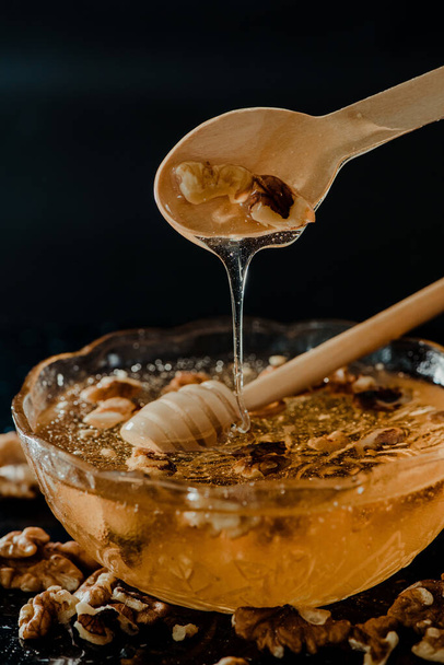 O mel em uma tigela de vidro com colheres de madeira nele pingando lentamente e decorado com nozes - Foto, Imagem
