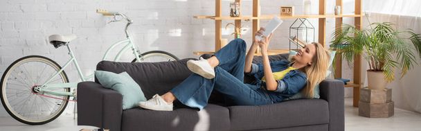 Sorrindo jovem olhando para tablet digital durante videochamada no sofá em casa, banner - Foto, Imagem