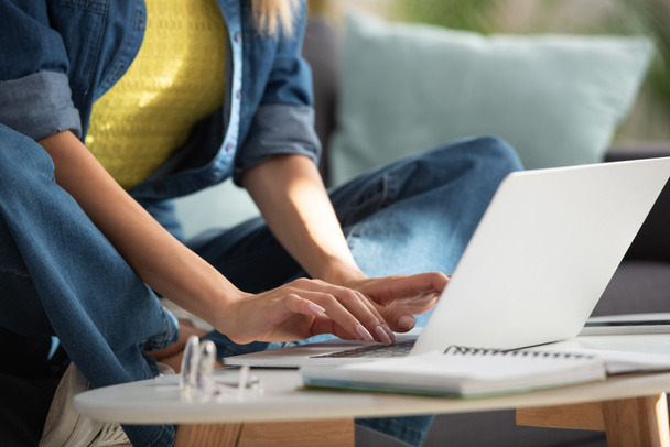 Gesneden weergave van jonge vrouw typen op laptop op wazig voorgrond thuis - Foto, afbeelding