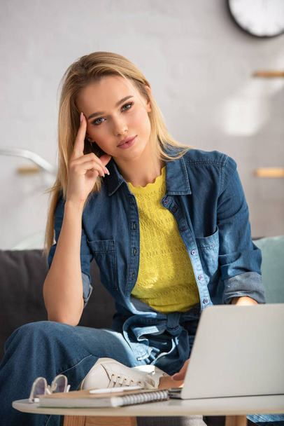 Young blonde woman looking at camera while sitting on couch at home on blurred background - Φωτογραφία, εικόνα