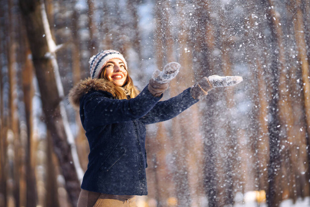 Happy winter time. Cute woman playing with snow  in snowy forest. Young lady in winter clothes enjoying the winter. Winter holiday. - Photo, Image