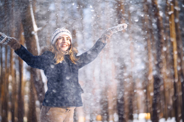 Happy winter time. Cute woman playing with snow  in snowy forest. Young lady in winter clothes enjoying the winter. Winter holiday. - 写真・画像