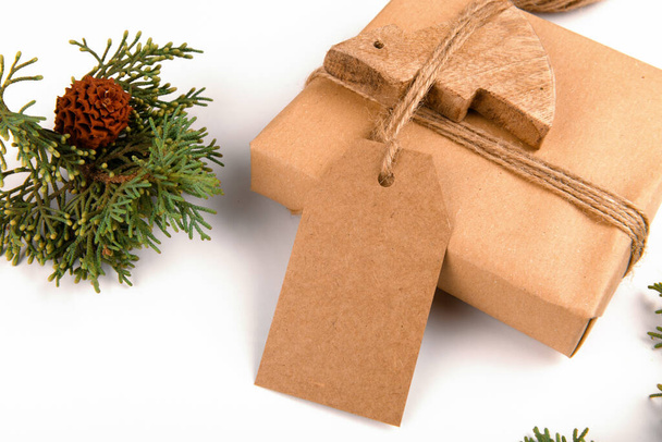 Різдвяна подарункова коробка наклеюється подарунковою коробкою, загорнутою в ремісничий перероблений папір з мотузкою та сосновими шишками з гілочками ялинки на білому тлі. Різдвяний або новорічний подарунок, місце для копіювання
 - Фото, зображення