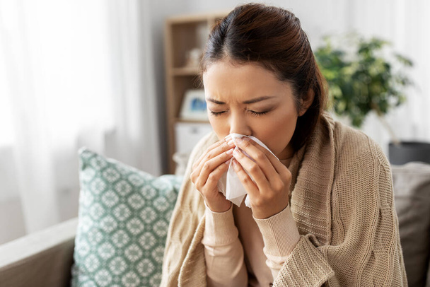 sick woman blowing nose in paper tissue at home - Photo, image