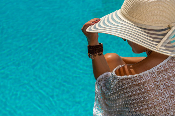 γυναίκα με ψάθινο καπέλο σε πολυτελές θέρετρο πέντε αστέρων δίπλα στην πισίνα.  - Φωτογραφία, εικόνα