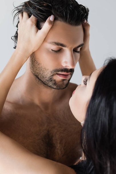 Mujer joven tocando la cabeza del novio sin camisa con los ojos cerrados aislados en gris  - Foto, Imagen