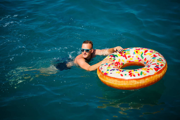 Nuori mies puhallettava rengas meressä lepää ja ui aurinkoisena päivänä - Valokuva, kuva