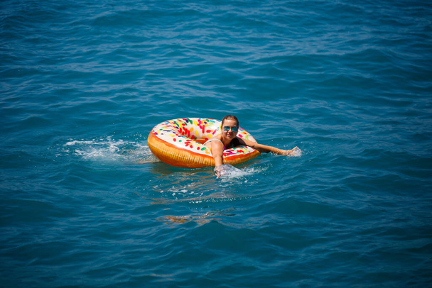 Krásná mladá žena v moři plave na nafukovacím prstenu a baví se na dovolené. Dívka v jasných plavkách u moře pod slunečním světlem - Fotografie, Obrázek