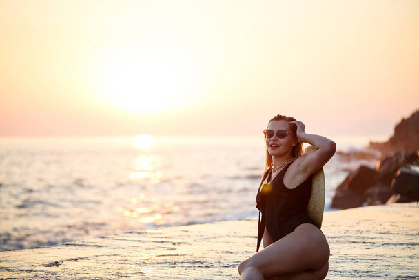 Kaunis nainen mustassa uimapuvussa meren rannalla, hymyilevät kasvot. Kultainen auringonlasku valo - Valokuva, kuva