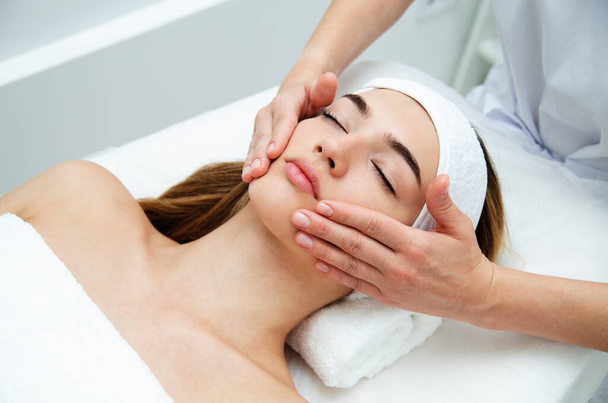 Beautician massaging woman's face. Attractive girl having facial treatment and massage. The young woman is lying and relaxingin. Beautiful female face receiving skin theraph - Fotoğraf, Görsel