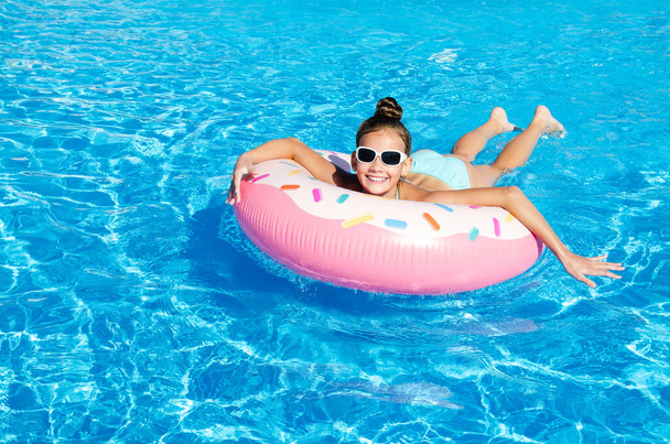 Cute smiling little girl in swimming pool with rubber ring. Child having fun on vacation in summertime - Foto, imagen