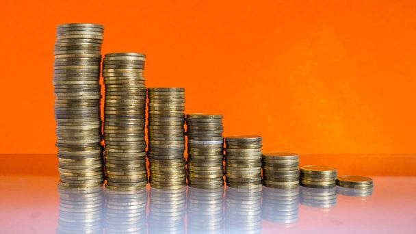 Stapeln von Münzen mit sinkenden Zinsen auf orangefarbenem Hintergrund.  - Foto, Bild