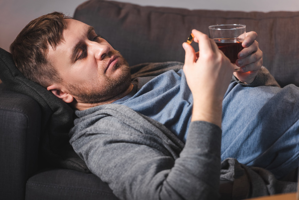 Depressiver Mann mit Ehering und Glas Whiskey auf Sofa liegend - Foto, Bild