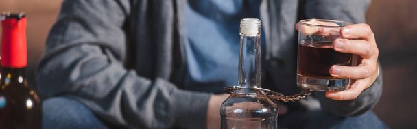 abgeschnittene Ansicht eines Mannes, gefesselt an eine Flasche, mit einem Glas Whiskey, Banner - Foto, Bild
